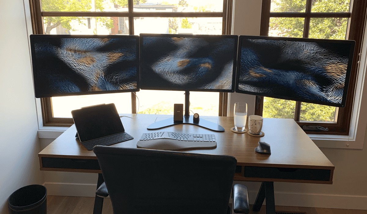 Desk with 3 monitors, iPad, mouse and keybaord